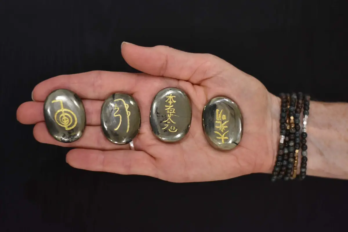 Her open palm holding four polished stones, each engraved with a Reiki symbol